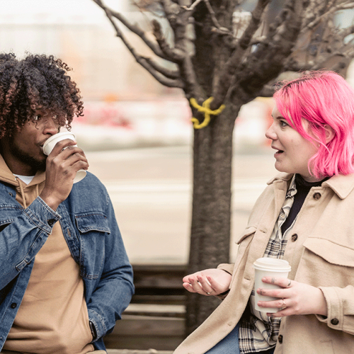 Young man and women talk on park bench drinking coffee