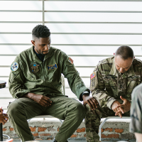 Two soldiers sitting, one visibly upset is comforted by the other